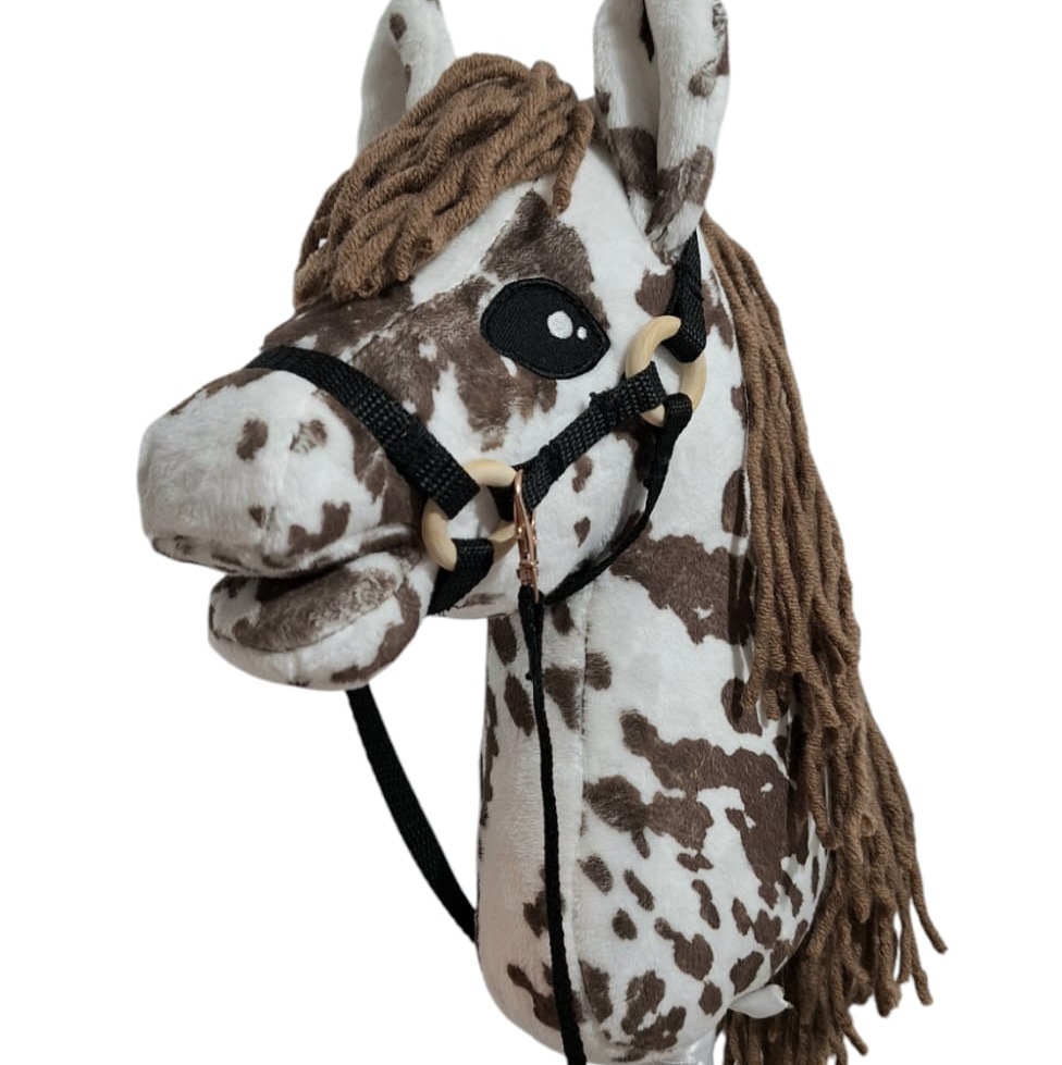 Pluszowy koń na kiju w brązowe łaty, z brązową grzywą i czarnym ogłowiem. Zabawka wykonana z dbałością o detale, na białym tle.