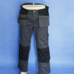 Szare spodnie robocze z czarnymi wzmocnieniami na kolanach i kieszeniami na wysokości pasa, prezentowane na manekinie na tle niebieskiego tła.