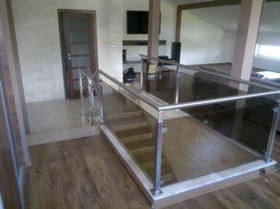 Wewnętrzne schody z drewnianymi stopniami i balustradą ze stali nierdzewnej oraz szkła, widok z góry na dół, nowoczesny design.