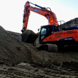 Pomarańczowa koparka Doosan DX300LC nabiera ziemię z hałdy podczas prac ziemnych, widoczne ślady gąsienic i warstwowa struktura wykopu.