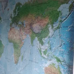 Ściana pokryta fototapetą z mapą świata, widoczne szczegóły kontynentów i oceanów, delikatne załamania fototapety w górnym rogu.