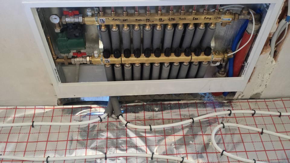 Rozdzielacz ogrzewania podłogowego z widocznymi rurami na folii izolacyjnej z rastrem, zamocowanymi opaskami zaciskowymi, w trakcie montażu.