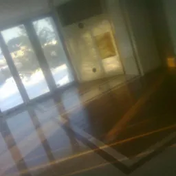 Wykończona podłoga z paneli w pomieszczeniu z dużym oknem balkonowym, przez które widać zimowy krajobraz. Ciemne panele ułożone we wzór, odbijają światło.