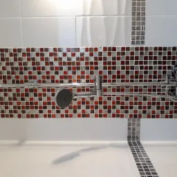 Wykończona łazienka z armaturą prysznicową na tle mozaiki w odcieniach brązu i czerwieni, z widoczną białą wanną i fragmentem ściany wyłożonej białymi płytkami.