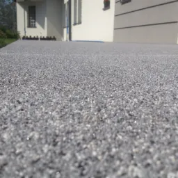 Szara, drobnoziarnista powierzchnia zewnętrzna z widocznym budynkiem w tle, wykonana w technologii bezspoinowej.