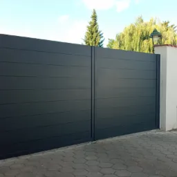 Nowoczesna, przesuwna brama aluminiowa ALUgate BORDER w kolorze grafitowym, z poziomymi panelami, zamontowana na posesji z kostką brukową i oświetleniem zewnętrznym.