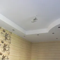 Wykończone wnętrze łazienki z podwieszanym sufitem z oświetleniem punktowym i częściowo położoną tapetą w kwiaty, widoczne kable wystające z otworu po lampie.