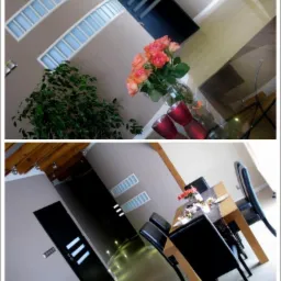 Dwupoziomowe wnętrze: na górze bukiet róż na szklanym stole, na dole jadalnia z drewnianym stołem i czarnymi krzesłami, czarne drzwi z białymi paskami.