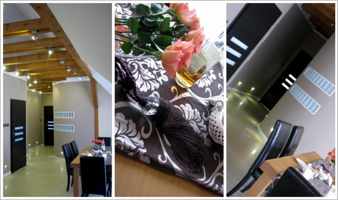 Nowoczesne wnętrze z drewnianymi belkami stropowymi i oświetleniem punktowym, widok na stół z dekoracją kwiatową i ozdobnym chwostem, czarne drzwi z białymi paskami w tle.