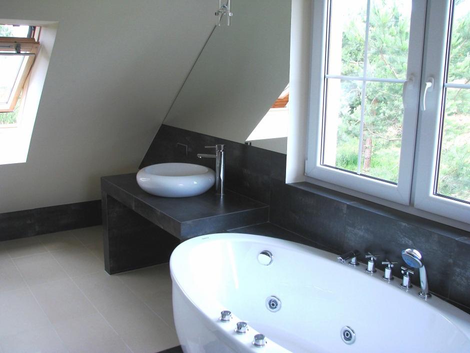 Nowoczesna łazienka na poddaszu z owalną umywalką na ciemnym blacie, białą wanną z hydromasażem i dużym oknem z widokiem na zieleń.