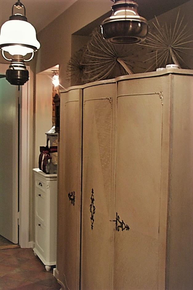 Antyczna szafa trzydrzwiowa w przedpokoju z dekoracyjnymi aplikacjami, ozdobiona suszonymi kwiatami i oświetlona wiszącymi lampami w stylu vintage.