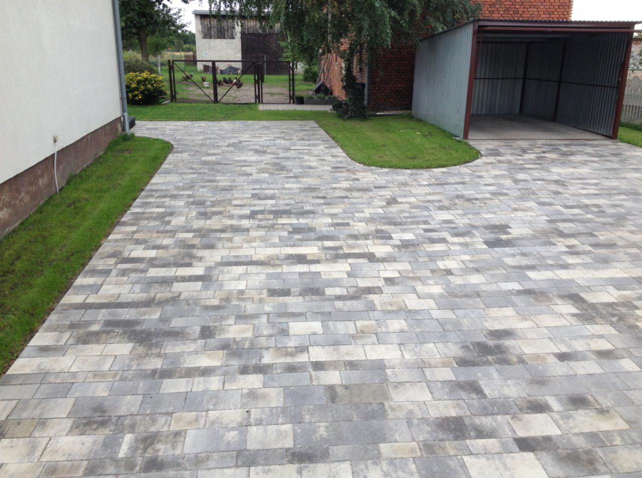 Ułożona szara kostka brukowa prowadząca do garażu w Tarnowskich Górach, z widocznym trawnikiem po bokach i budynkami w tle.