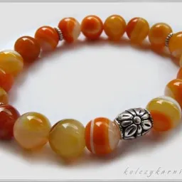 Bransoletka z agatów w odcieniach pomarańczy i żółci, z srebrnymi przekładkami w kształcie kwiatów, ułożona na białym tle.