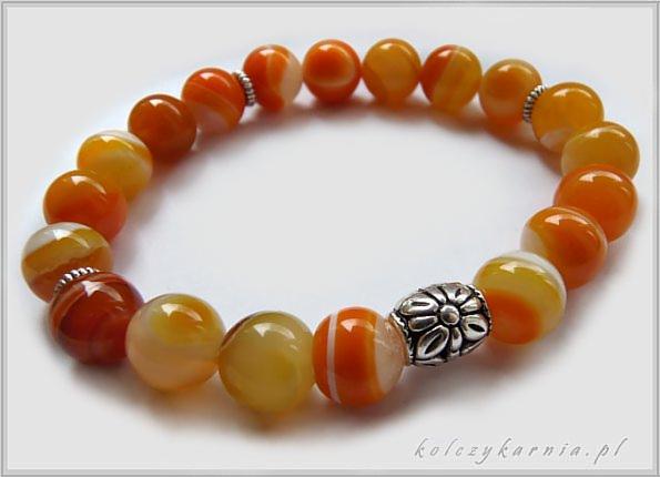Bransoletka z agatów w odcieniach pomarańczy i żółci, z srebrnymi przekładkami w kształcie kwiatów, ułożona na białym tle.