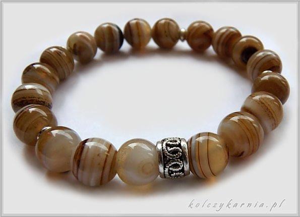 Bransoletka z okrągłych, polerowanych agatów w odcieniach beżu i brązu, z ozdobnym, srebrnym elementem pośrodku, na białym tle.