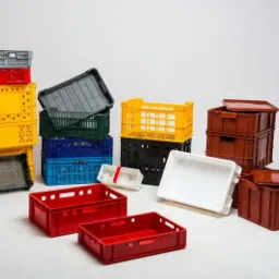 Różnokolorowe skrzynki z tworzywa sztucznego, niektóre perforowane, ułożone w stosy i pojedynczo na białym tle, prezentujące różnorodność kształtów i rozmiarów.
