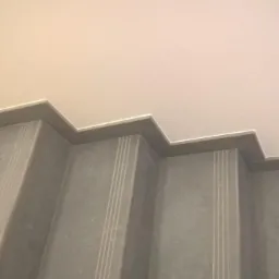 Schody wykończone szarymi płytkami z trzema pionowymi rowkami na każdym stopniu, widok z dołu na sufit.