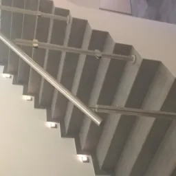 Betonowe schody z oświetleniem punktowym na stopniach i metalową balustradą, widok z dołu pod kątem.