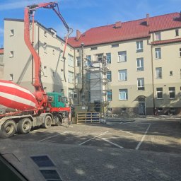 PHU Łącznik II Piotr Łączyński - Betonomieszarka z pompą podaje beton na rusztowanie przy budynku w Ustce, widoczne prace murarskie na wysokości.