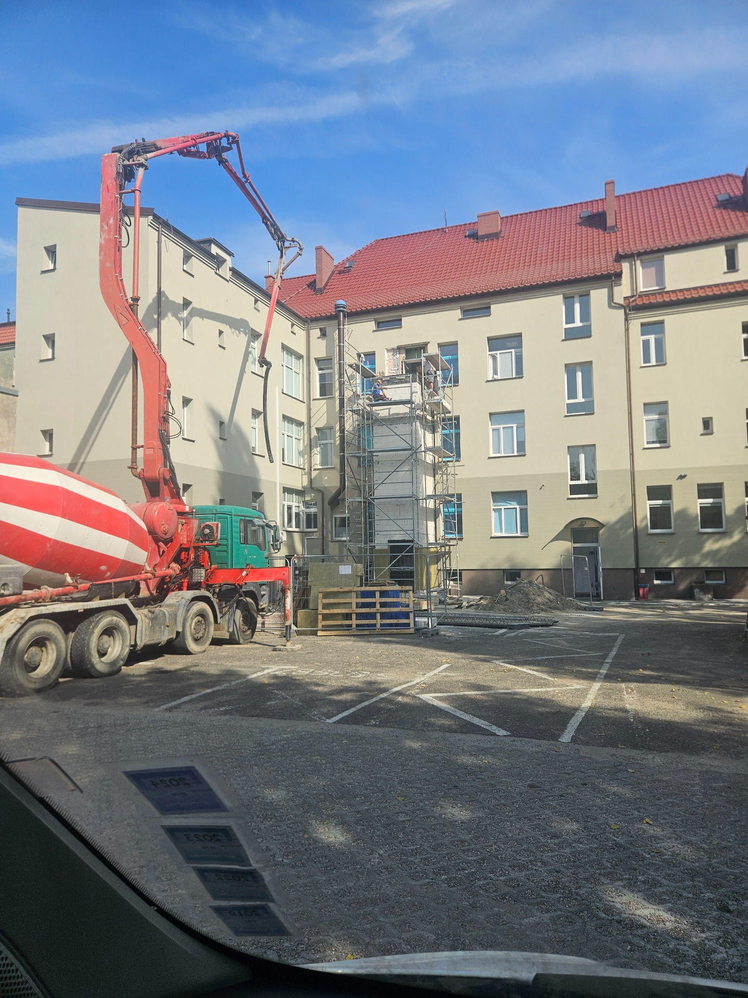 Betonomieszarka z pompą podaje beton na rusztowanie przy budynku w Ustce, widoczne prace murarskie na wysokości.