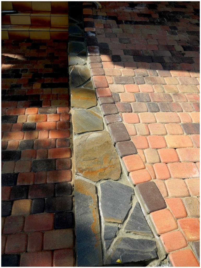 Kolorowa kostka brukowa ułożona obok schodów z cegły i kamiennej obudowy. Cień podkreśla fakturę nawierzchni. Widok z góry.