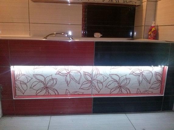 Umywalka w łazience z podświetlanym panelem dekoracyjnym z motywem kwiatowym na czerwono-czarnym tle płytek.