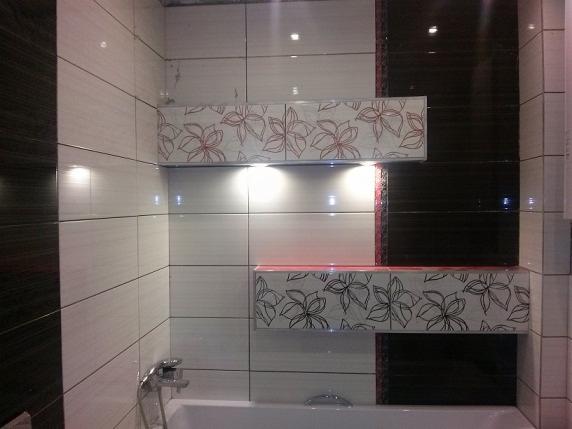 Wykończona łazienka z białymi i czarnymi płytkami, dekoracyjne półki z motywem kwiatowym, oświetlenie punktowe nad wanną.