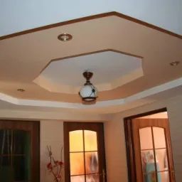 Oryginalny sufit podwieszany z oświetleniem punktowym i centralną lampą, wykończony w odcieniach beżu i brązu, widoczne drzwi z szybami w tle.