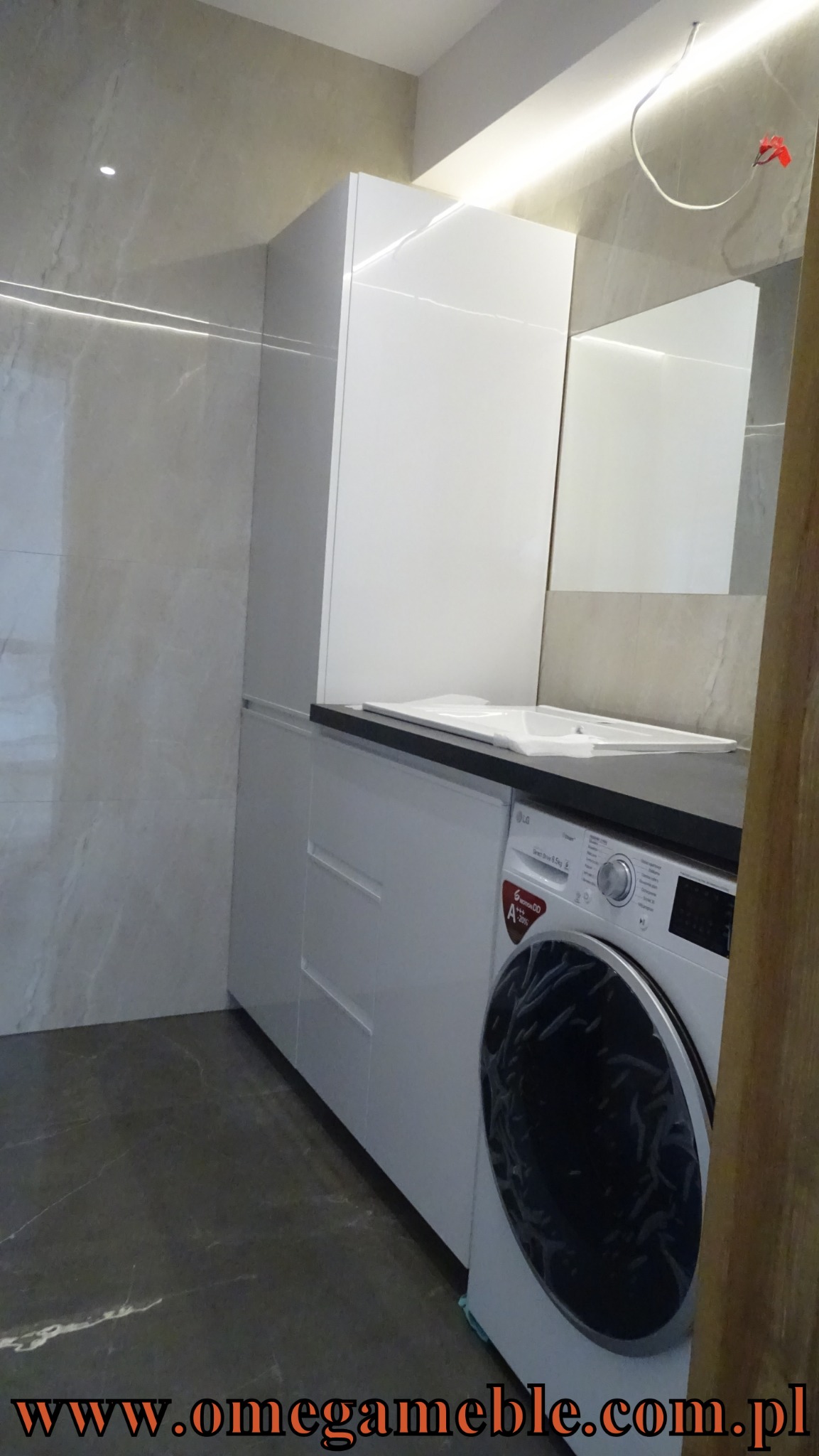 Biała zabudowa meblowa w łazience z pralką LG, marmurowe ściany i podłoga, oświetlenie LED podszafkowe.