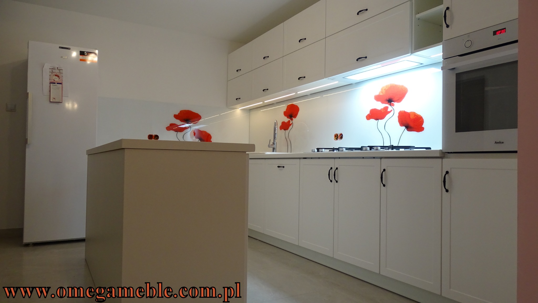 Nowoczesna, biała kuchnia z wyspą, fronty zdobione motywem czerwonych maków, oświetlenie LED pod szafkami wiszącymi, zabudowa piekarnika.