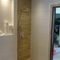 Nowoczesna łazienka po remoncie: białe płytki, drewnopodobne panele ścienne w strefie prysznica z deszczownicą, podłoga z drewnopodobnych paneli z dekoracyjnym czarno-białym obramowaniem, wnęka...