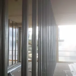 Konstrukcja ścian działowych z profili stalowych w surowym stanie, widok z dołu. Na podłodze leżą profile, w tle okno i drabina.