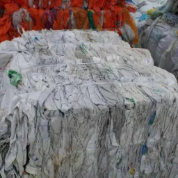 Stos sprasowanych, zużytych worków typu BIG BAG, związanych sznurkiem, z widocznymi zabrudzeniami i resztkami zawartości, obok sterty kolorowych siatek.