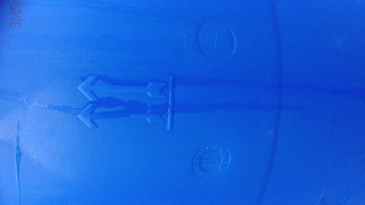 Fragment niebieskiej plastikowej beczki z wytłoczonymi symbolami recyklingu i strzałką wskazującą kierunek układania.