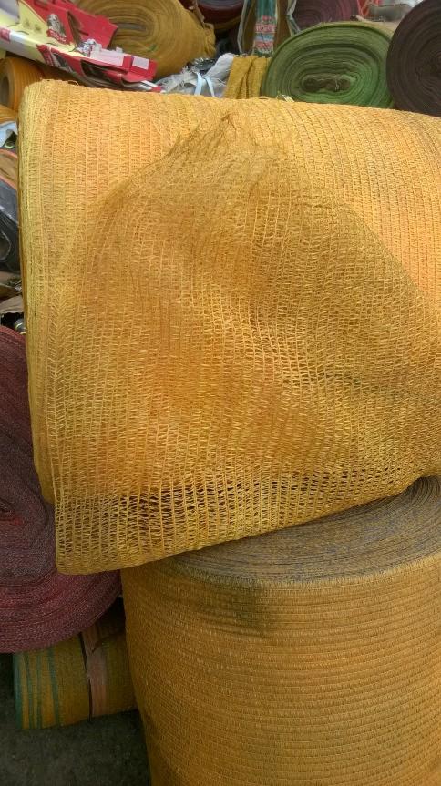 Zrolowana, pomarańczowa siatka PP poprodukcyjna o widocznej strukturze oczek, leżąca na innych rolkach materiałów.