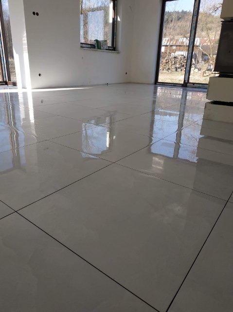 Błyszcząca, jasna podłoga z płytek w nowym, pustym pomieszczeniu z dużymi oknami i widokiem na zewnątrz.