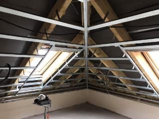 Stelaż sufitu podwieszanego z profili metalowych w trakcie montażu, widoczne okno dachowe i przewody elektryczne.