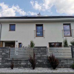 Cr-budsystem Robert Cendalski - Nowoczesny dom jednorodzinny z szarą, betonową podstawą ogrodzenia i poziomymi, metalowymi przęsłami, widoczne panele słoneczne na dachu.