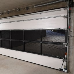 Cr-budsystem Robert Cendalski - Zamknięta, segmentowa brama z kratką wentylacyjną w garażu podziemnym, widoczne sprężyny i mechanizm otwierania.