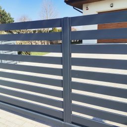 Cr-budsystem Robert Cendalski - Nowoczesna brama wjazdowa z poziomych, szarych profili, widok z zewnątrz na tle domu z czerwoną dachówką i jasną elewacją.