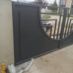 Cr-budsystem Robert Cendalski - Szara brama wjazdowa z automatyką, widoczny siłownik przy słupku, na podjeździe kostka brukowa, w tle samochód osobowy i budynek.