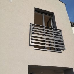 Cr-budsystem Robert Cendalski - Nowoczesny balkon z szarymi, poziomymi barierkami na tle jasnej elewacji budynku i błękitnego nieba.