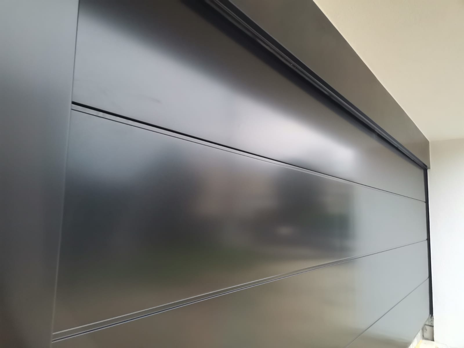 Brama o wymiarach 6000x2500m w kolorze czarnym RAL 9005, wpuszczana na zewnątrz do elewacji.