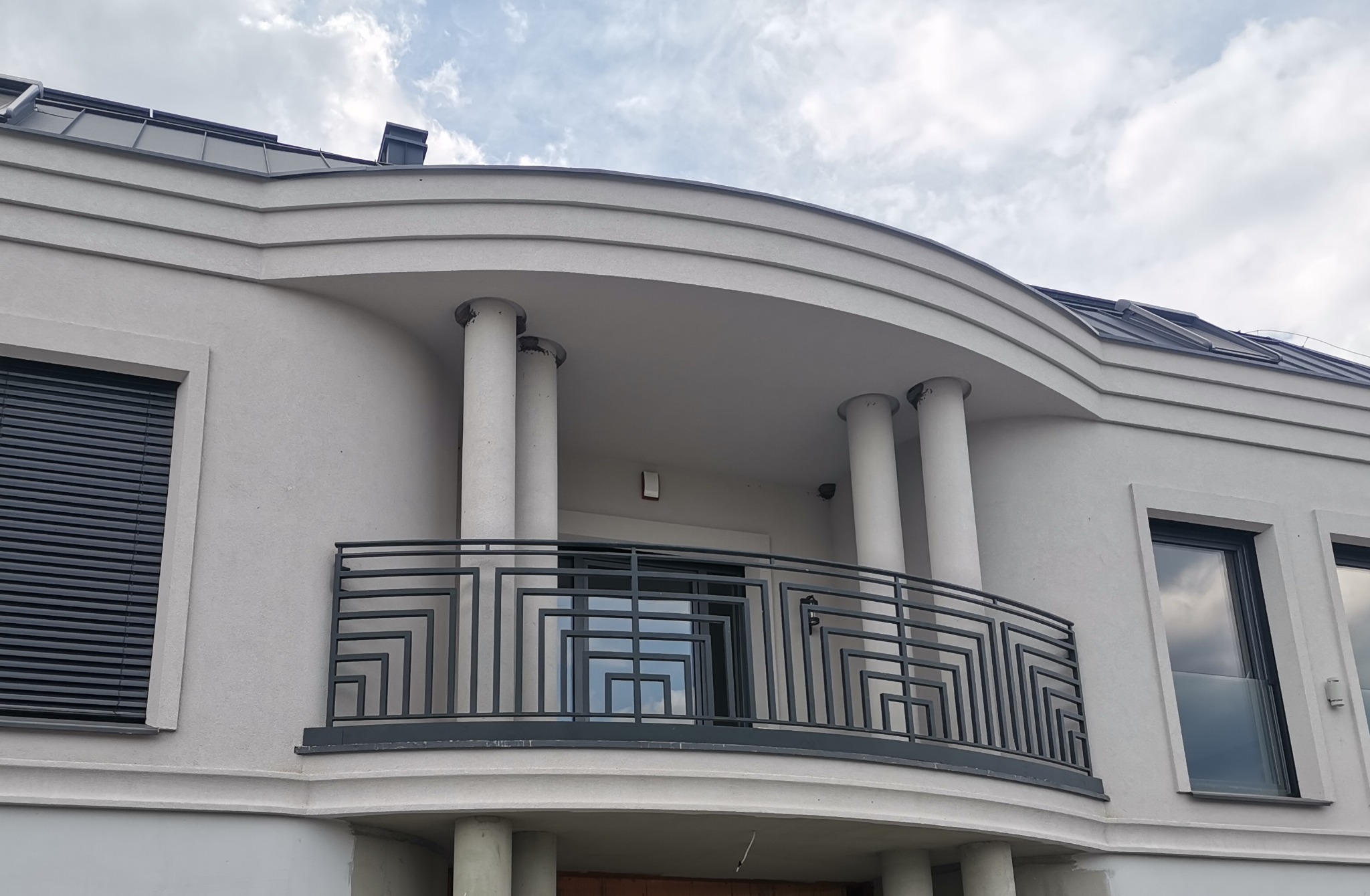 Elewacja budynku w Poznaniu z balkonem o nowoczesnej, geometrycznej balustradzie i kolumnami podtrzymującymi zadaszenie.