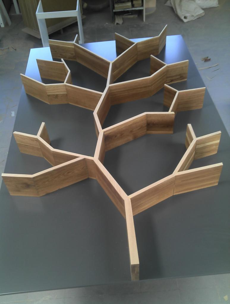 Kreatywny regał w kształcie drzewa, wykonany z jasnego drewna, na ciemnym tle. Nietypowy projekt z Wołomina, gotowy do montażu.