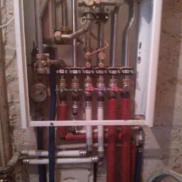 Zamknięta szafka z rozdzielaczem instalacji centralnego ogrzewania z rurami w kolorze czerwonym, białym i niebieskim na tle ściany z surowego betonu.