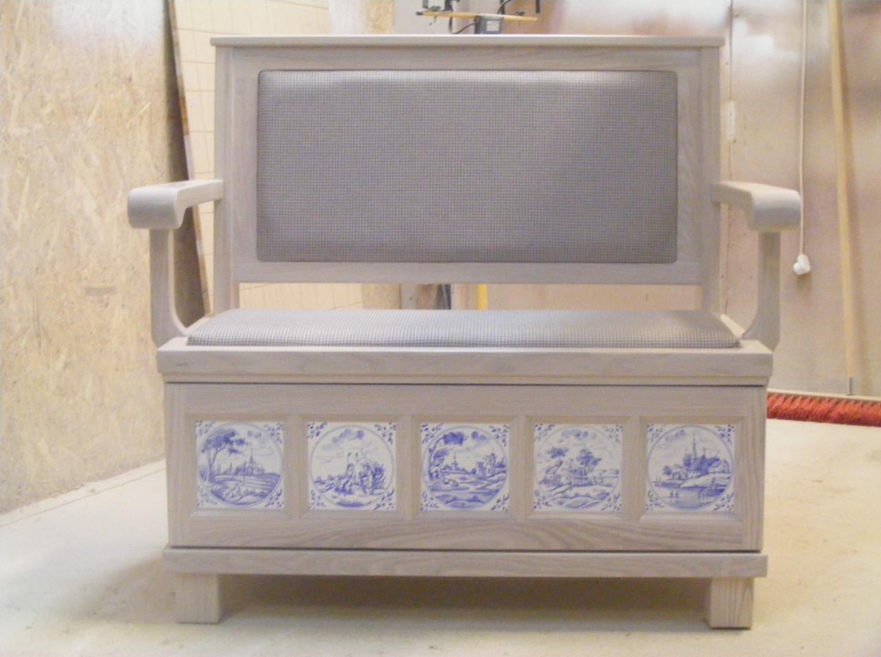 Drewniana ławka z oparciem, siedziskiem w kratę i zdobieniami z płytek ceramicznych z motywami krajobrazowymi. Wykończenie w jasnym odcieniu drewna.