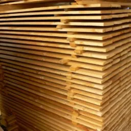 Stos desek ułożonych warstwami, widoczne słoje drewna i jasna barwa. Deski są świeżo przetarte i przygotowane do dalszej obróbki lub sprzedaży.