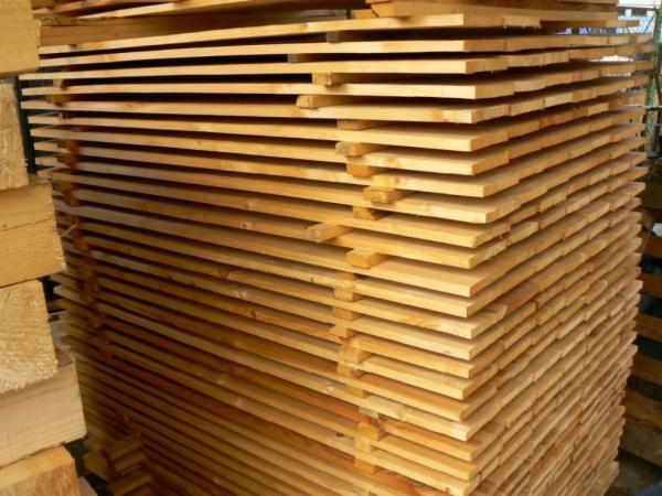 Stos desek ułożonych warstwami, widoczne słoje drewna i jasna barwa. Deski są świeżo przetarte i przygotowane do dalszej obróbki lub sprzedaży.