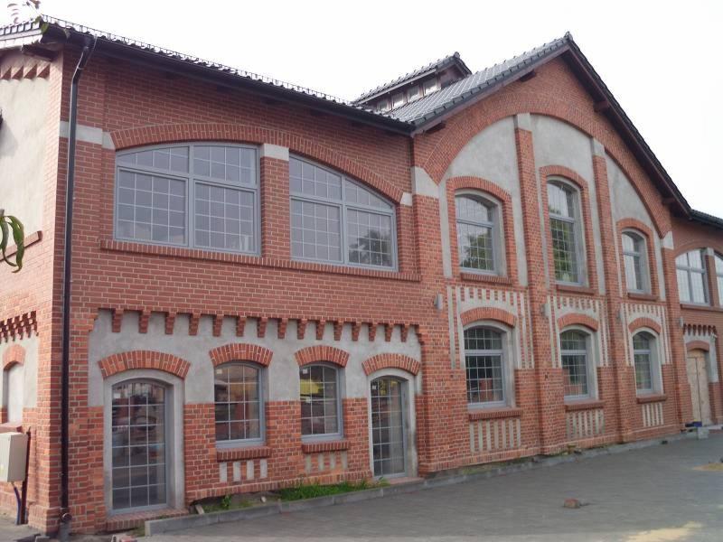 Fasada budynku z czerwonej cegły z szarymi oknami i dekoracyjnymi elementami z betonu, widok z zewnątrz.